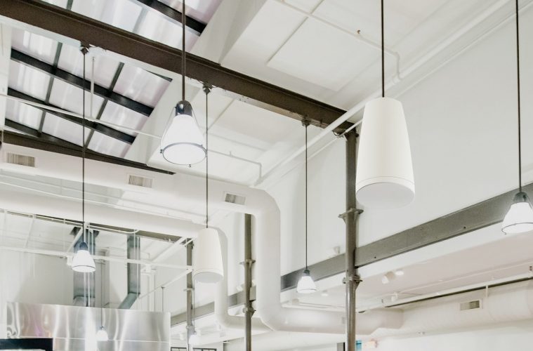 Industrial-style ceiling with exposed beams and multiple Sonance professional pendant speakers, highlighting a modern commercial audio setup.
