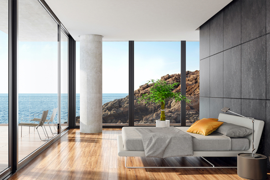 Contemporary bedroom with floor-to-ceiling windows and ocean view, featuring an invisible Sonance speaker installation.