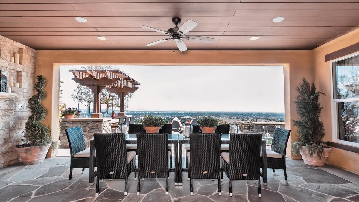 Elegant outdoor dining area with a long table and panoramic view, featuring Sonance outdoor speakers discreetly installed in the ceiling.