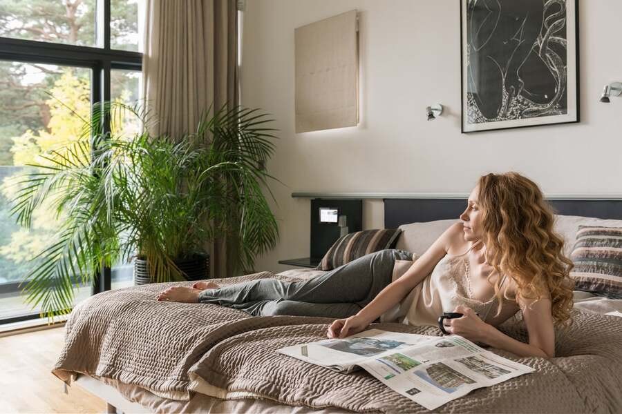 A woman rests in her luxury bedroom with a Crestron smart home system managing her surroundings.