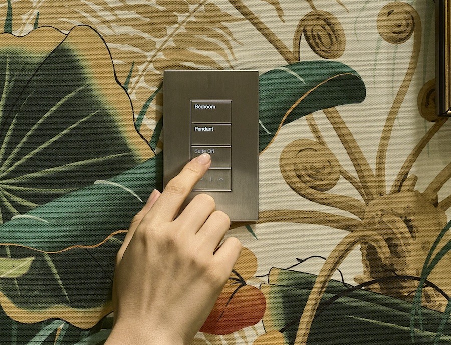 A hand tapping a button on a Lutron Palladiom keypad with a floral wallpaper background.