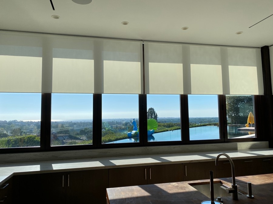 Modern kitchen with large windows featuring smart shades, overlooking a scenic view, with a sleek countertop and artistic decor.