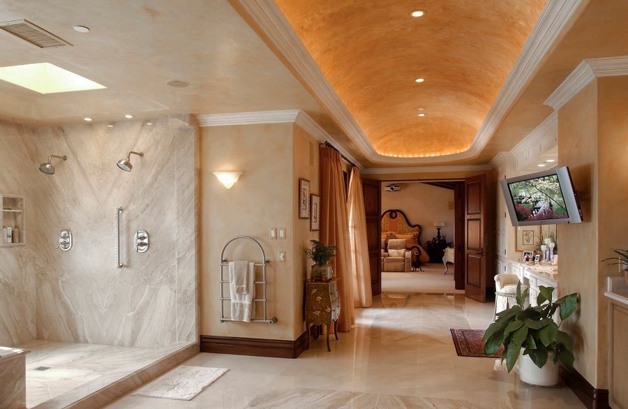 A master bathroom with soft golden ceiling lighting, various light fixtures, a TV, and in-ceiling speakers.