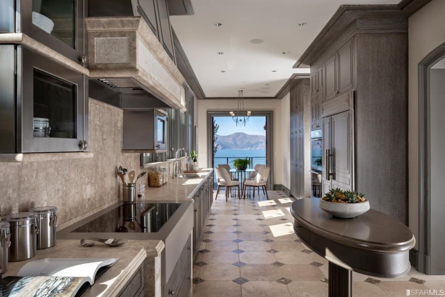 A long, elegant kitchen with in-ceiling speakers leading to a table overlooking the ocean.