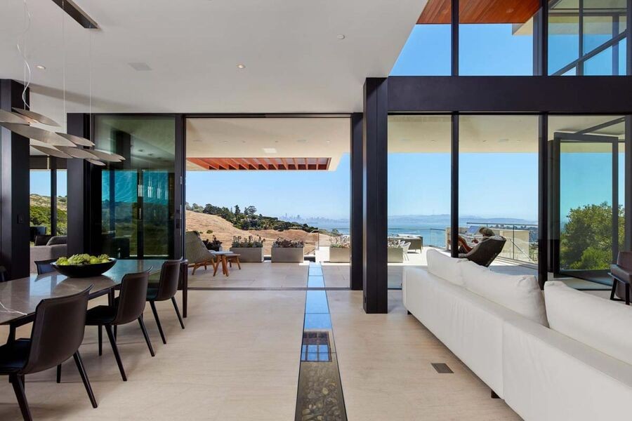 A luxury living space with a kitchen on one side and a living room on the other. On the back, a floor-to-ceiling window oversees the ocean.