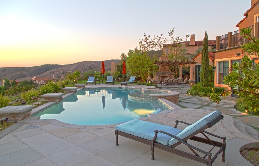 A beautiful backyard with pool and lounge chairs, and Sonance landscape speakers and subwoofer placed along the perimeter.