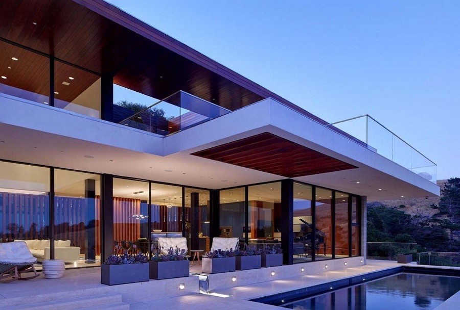 Sophisticated and elegant modernist home nestled in the hill with walls of windows and an illuminated pool.