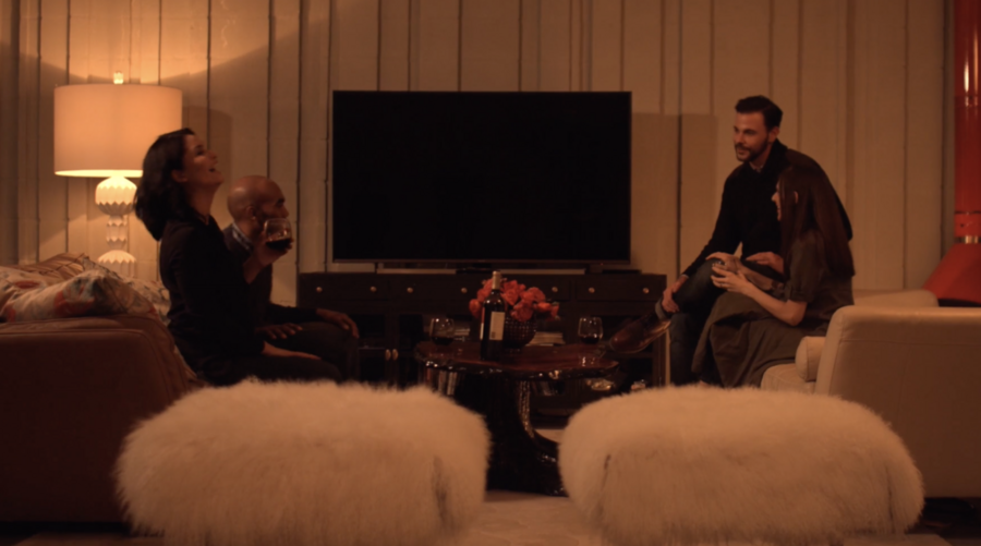 People sitting on couches around a coffee table, drinking and laughing. 
