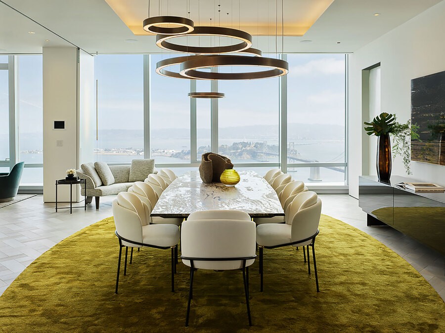 A luxury dining room overseeing a city. Above the dining table there is cove lighting glowing in an amber hue.