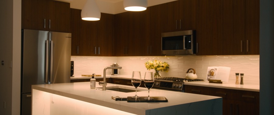 A modern kitchen with two wine glasses on the counter. Tunable lighting is set to a warm shade of white.