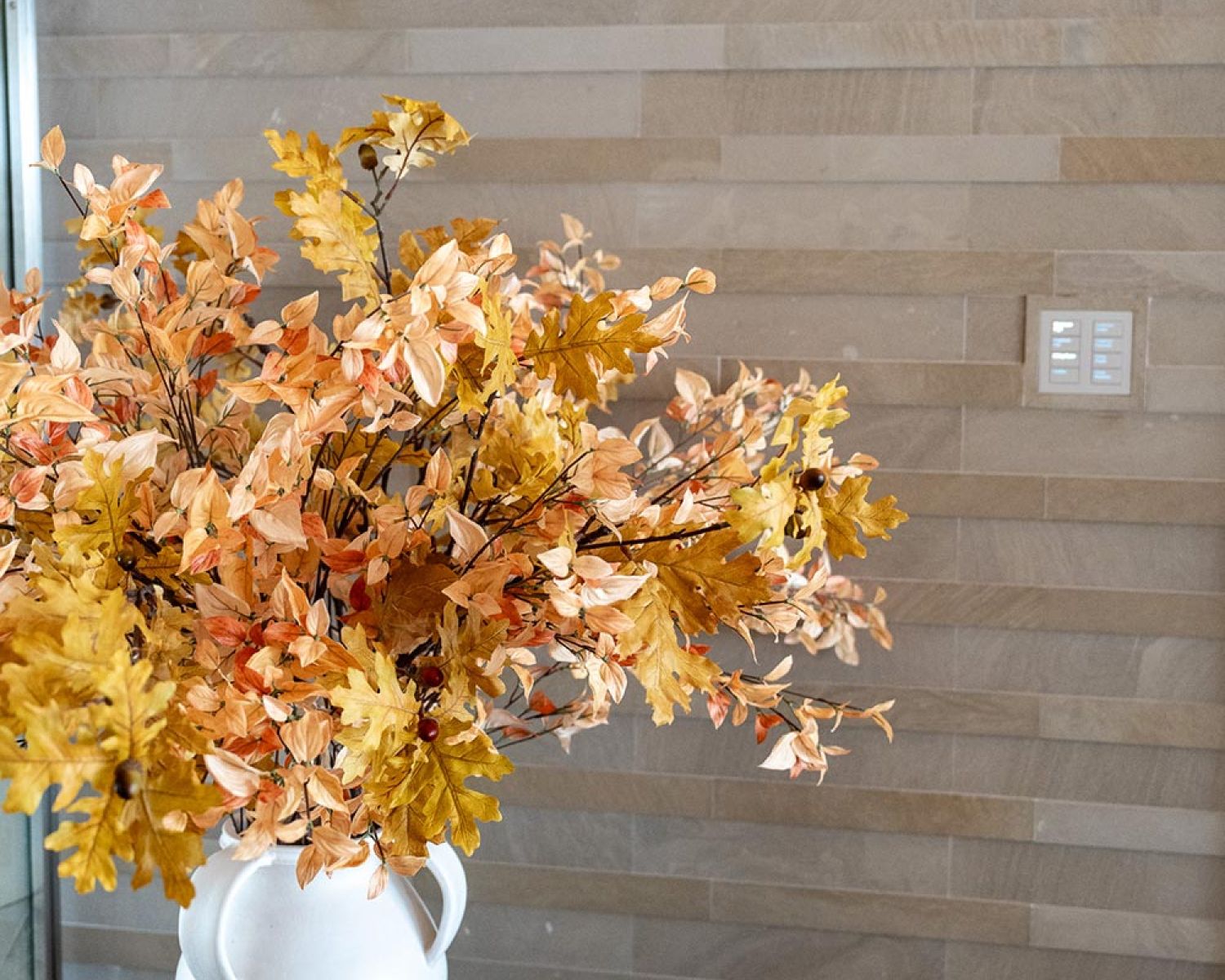 Decorative fall foliage arrangement in white vase on round table