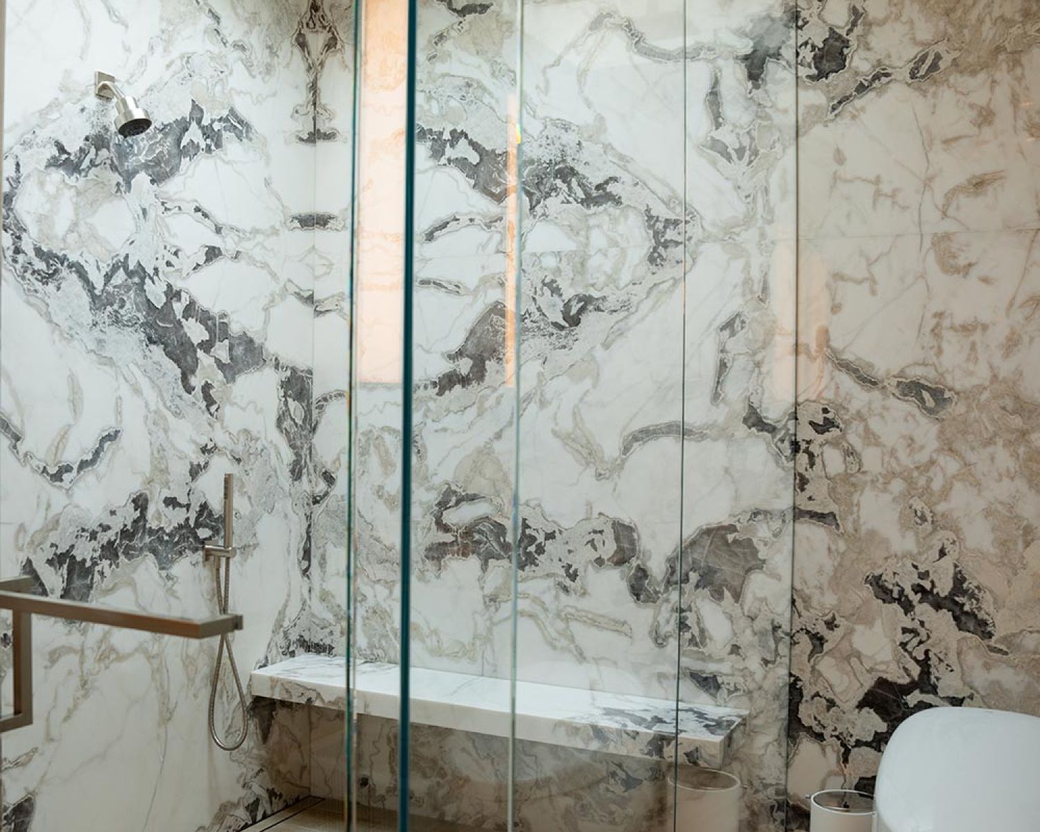 Glass enclosed shower with marble walls and skylight