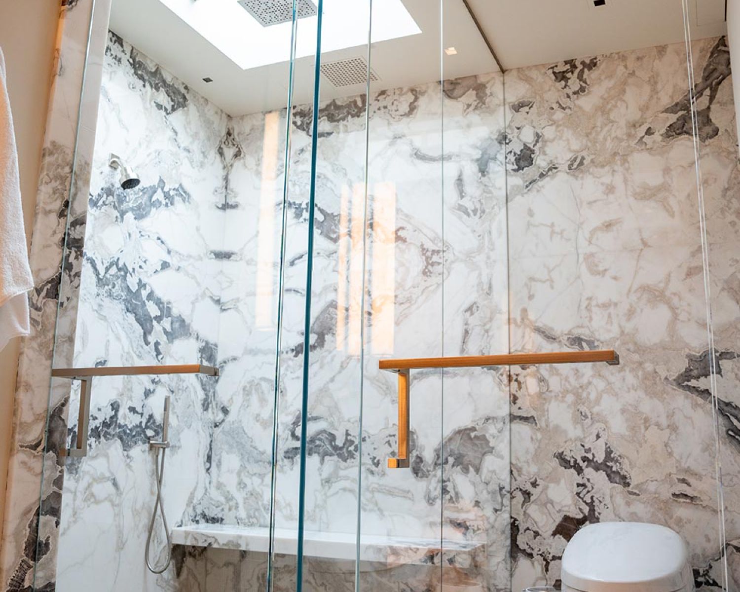 Glass enclosed shower with marble walls and skylight