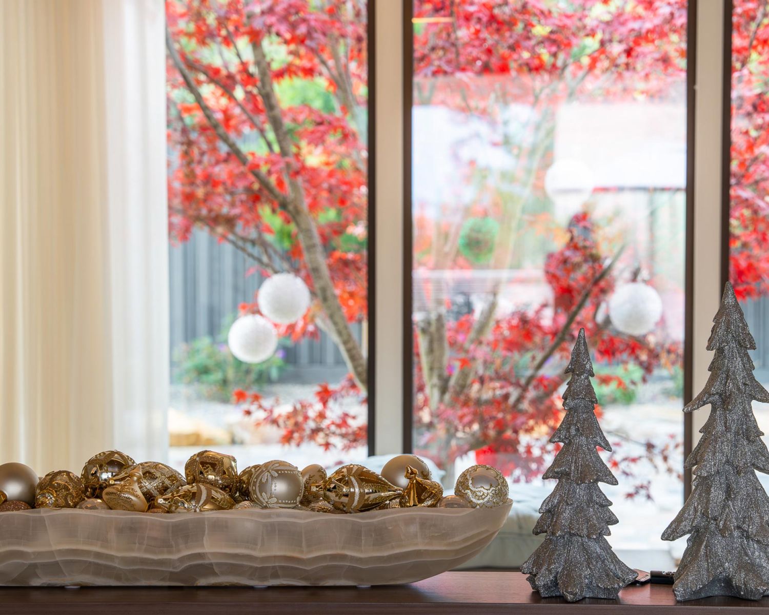 Decorative bowl with ornaments and holiday trees by window